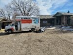 A moving truck parked outside a building, with bags on the ground.